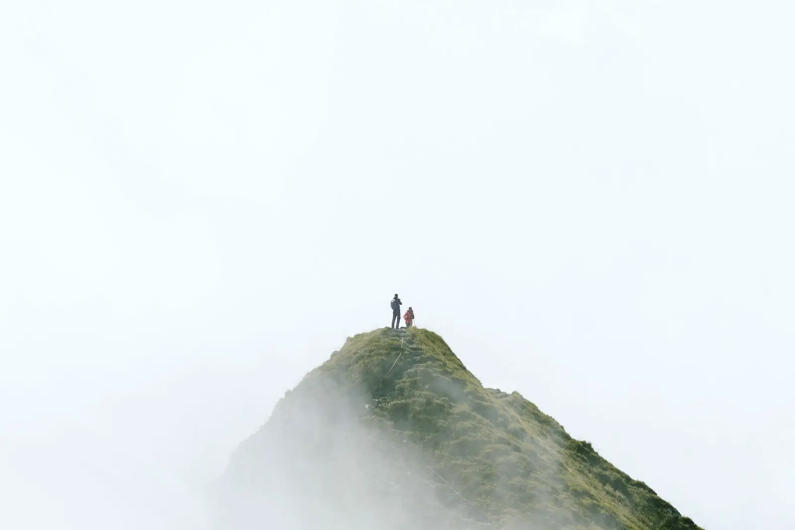 Two walkers on a grassy mountain ridge above the cloud